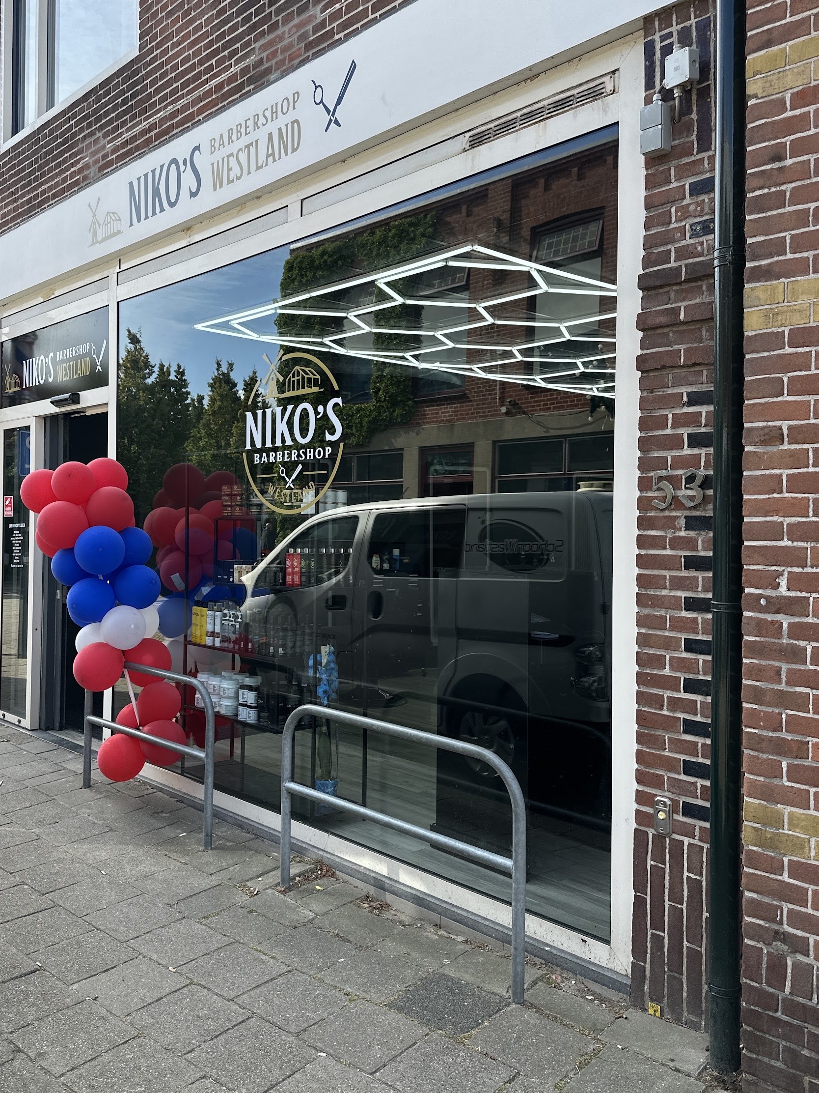 De winkelpui van Niko’s Barbershop aan de Voorstraat, met het lichtplafond achter het raam