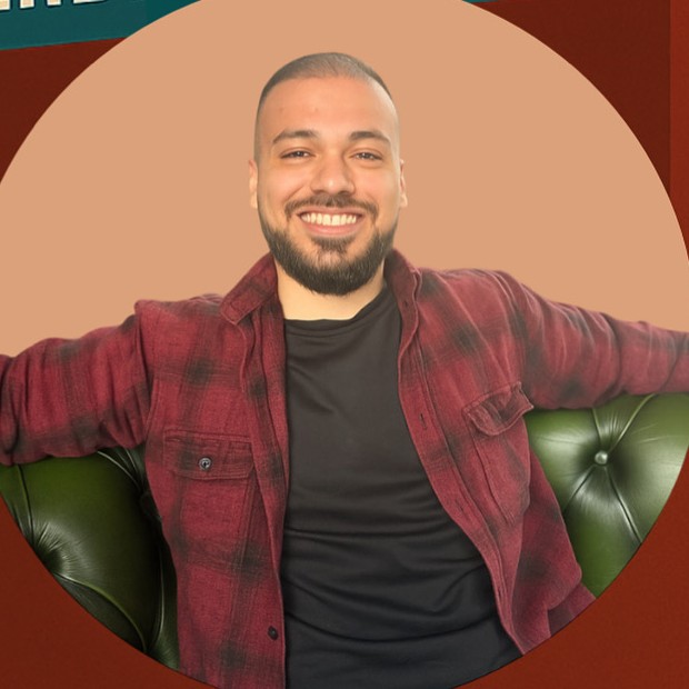 Niko, de eigenaar van Niko’s Barbershop, lachend in een geruit overhemd
