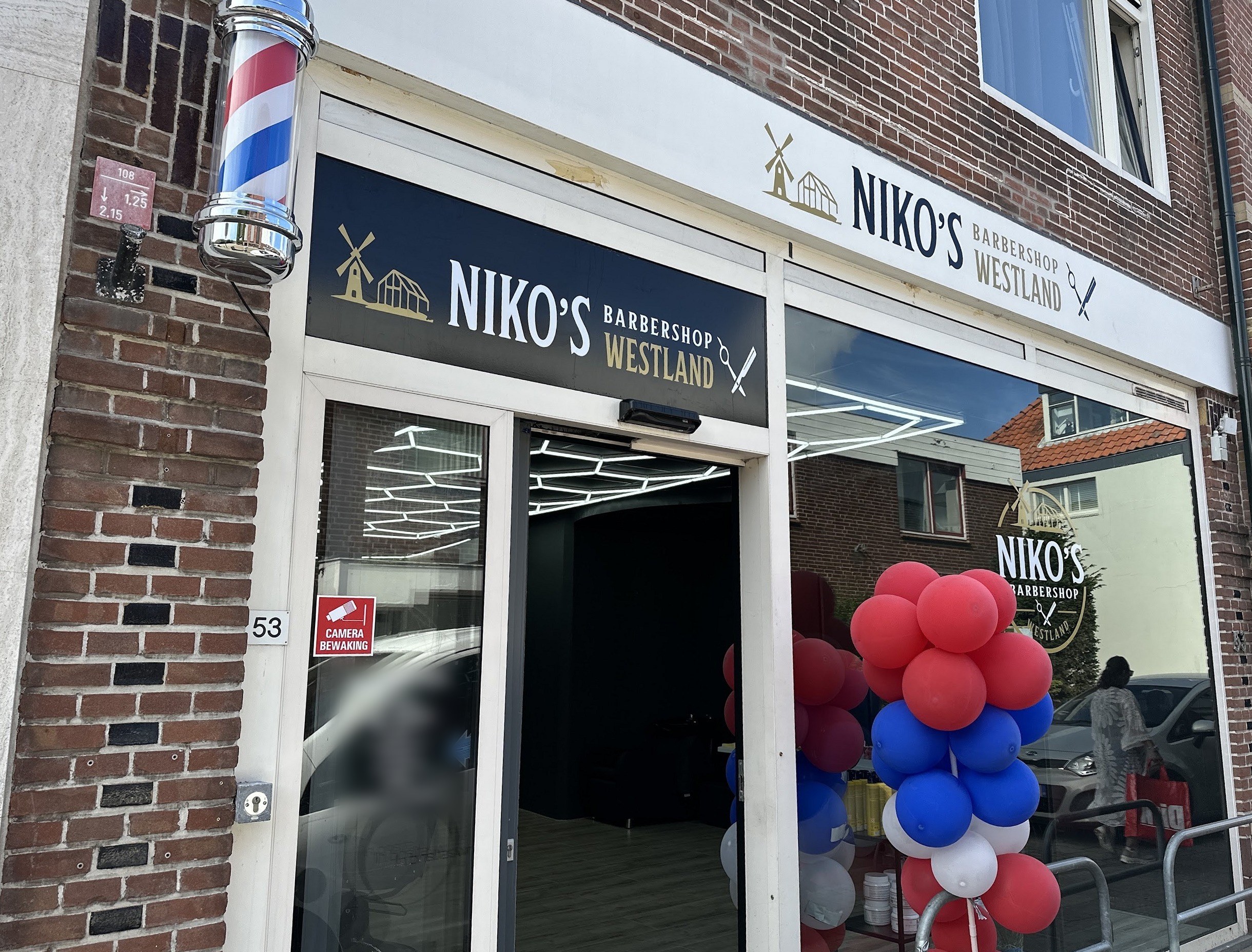 De gevel van Niko’s Barbershop aan de Voorstraat 53 in Poeldijk, met de barberpaal en de twee NIKO’S-borden